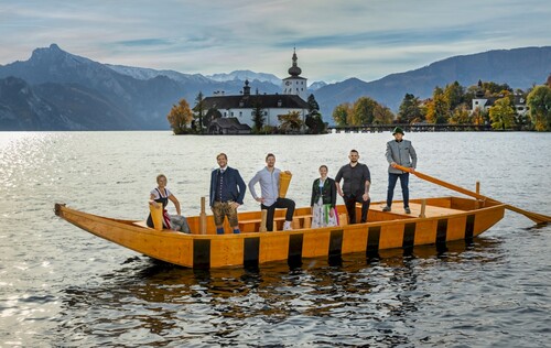 Sechs Personen in Trachtenkleidung auf einer großen Zille auf einem See, im Hintergrund Schloss Ort